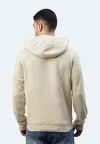 Felpa color crema con vestibilità rilassata, cappuccio regolabile con cordino e polsini a costine. Il tessuto appare morbido con una finitura testurizzata.