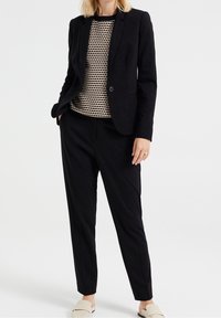 Svart skräddarsydd blazer och svarta byxor, kombinerat med en mönstrad stickad topp i kräm och svart. Slätt tyg med en strukturerad passform.