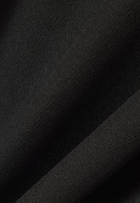 Gros plan sur un tissu noir texturé à tissage fin avec de subtiles plis diagonaux créant un contraste de lumière et d'ombre.