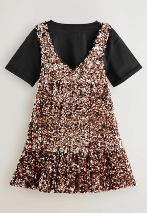 Abito senza maniche corto ricoperto di paillettes oro rosa indossato sopra una semplice maglietta nera a maniche corte.