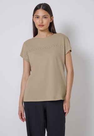 Beige top s krátkým rukávem a kulatým výstřihem, který zdobí vodorovný pruh malých dekorativních cvočků přes hruď. Měkká textura a volný střih.