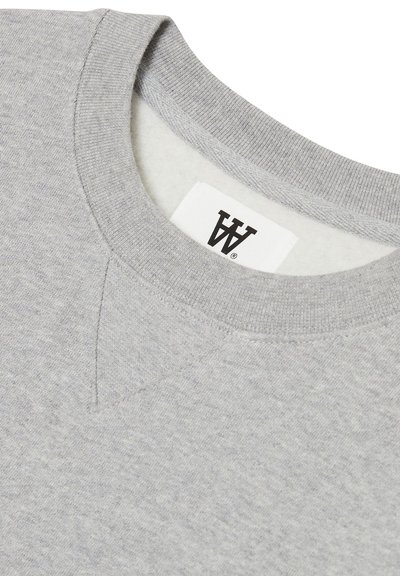 Světle šedá mikina s kulatým výstřihem, texturovaná tkanina a logo štítek přišitý uvnitř límce. Obsahuje jemný v-šev detail.