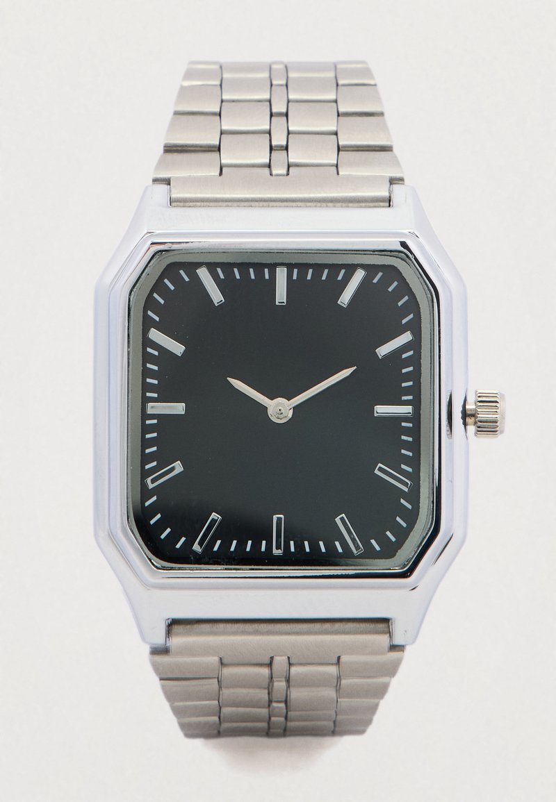 Ασημένιο τετράγωνο ρολόι με μαύρο καντράν, ασημένιους δείκτες ώρας και μεταλλικό μπρασελέ με κρίκους. Δείχνει μίνιμαλ σχεδιασμό και απλές λεπτομέρειες.