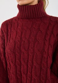 Maglione rosso a collo alto in tessuto cable-knit con colletto a costine e motivo testurizzato, realizzato in un filato spesso e morbido per calore e comfort.