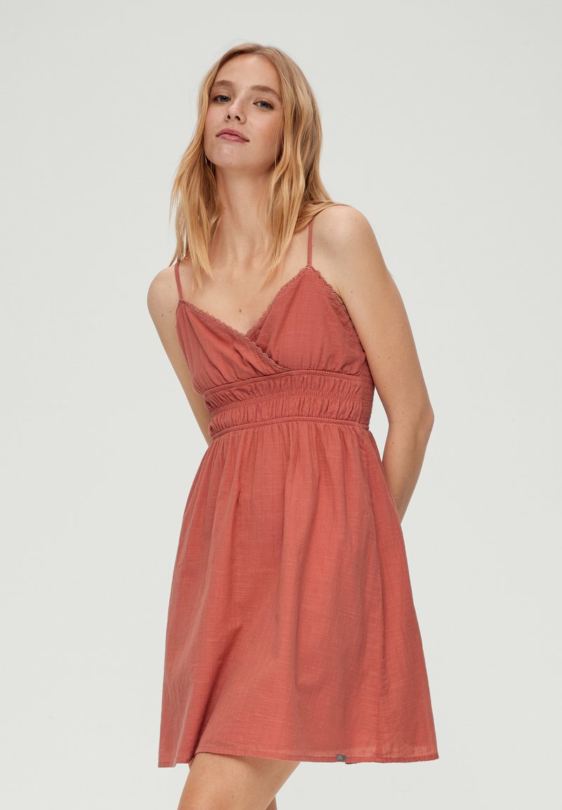 Roze-rode jurk met een wikkelontwerp, verstelbare spaghettibandjes, gesmokt taille en een vloeiende rok. Textiel met textuur voor een zachte uitstraling.