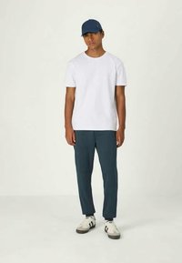 White crew-neck t-shirt, dark blue pants, blue cap, and white sneakers with black accents. Set against a neutral background.