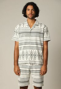 Korte mouwen overhemd en bijpassende shorts in een zwart-wit geometrisch patroon. Zacht materiaal met een relaxte pasvorm en knoopsluiting.