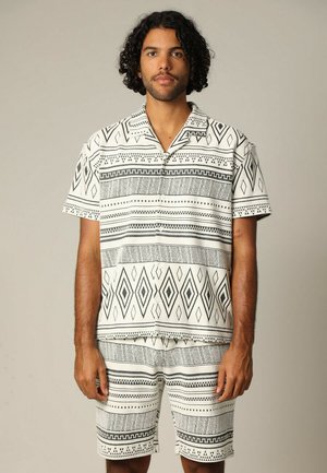 Korte mouwen overhemd en bijpassende shorts in een zwart-wit geometrisch patroon. Zacht materiaal met een relaxte pasvorm en knoopsluiting.