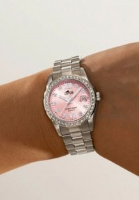 Montre en acier inoxydable argenté avec un cadran rose, des accents en cristal, des chiffres romains et un affichage de la date. Bracelet de style montre.