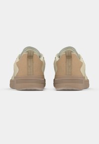 Baskets beiges avec un dos texturé, des côtés lisses et un tirant de talon renforcé. La semelle est marron clair avec des rainures horizontales.