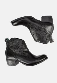 Las botas de tobillo de cuero negro presentan patrones florales perforados, un tacón bajo apilado y un cierre lateral con cremallera. Tienen una textura suave en todo su diseño.