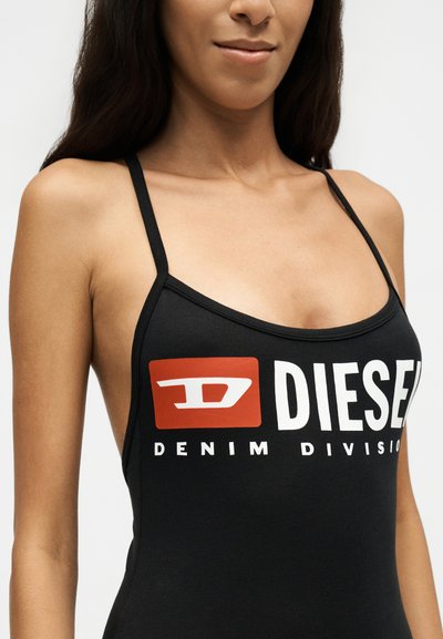 Жена, носеща черен топ с тънки презрамки и бяло-червено лого Diesel Denim Division на гърдите.