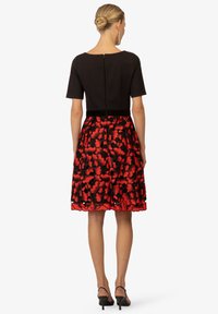 Schwarz-rotes Blumenkleid mit einem taillierten Oberteil, kurzen Ärmeln, einem strukturierten Taillenbund und einem ausgestellt Rock mit gewelltem Saum.