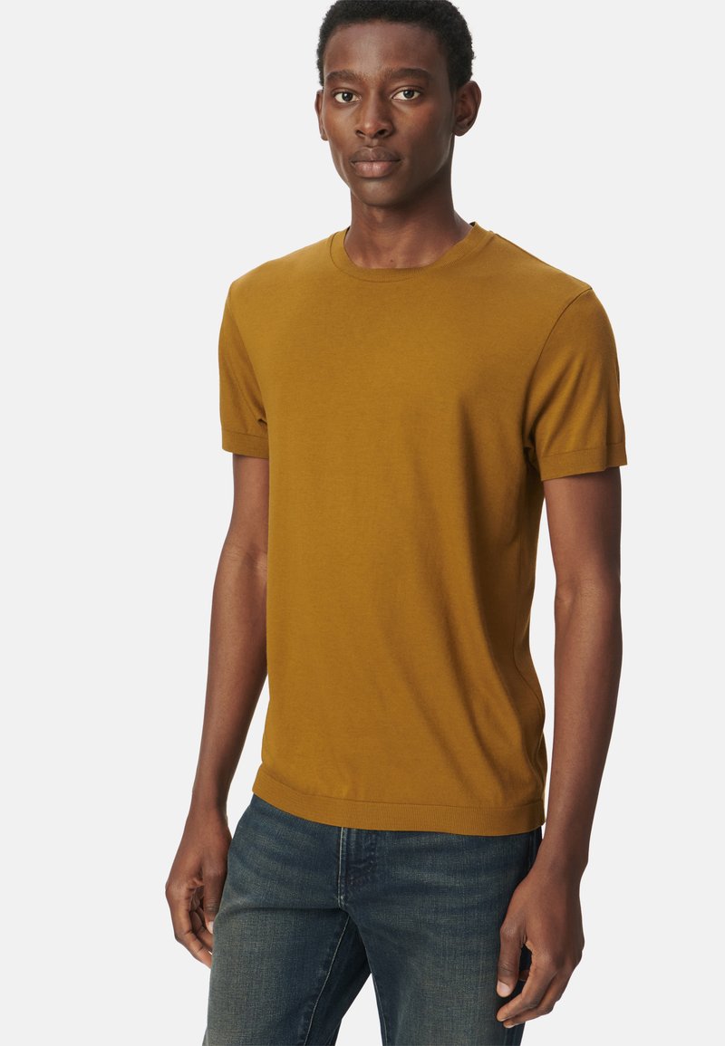 T-shirt a maniche corte giallo senape con scollatura rotonda, realizzato in tessuto morbido, con un design aderente e sottili accenti a costine sulle maniche.