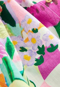 Fabric with colorful floral print featuring purple flowers, green leaves, and pink and white background details.