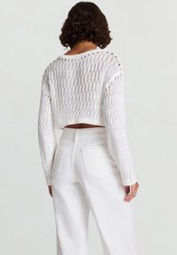 Maglione bianco corto in maglia con motivo a trama aperta, maniche lunghe e scollo a coste. Abbinato a pantaloni bianchi a vita alta.