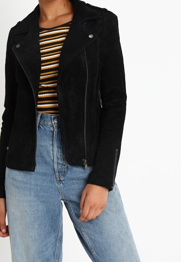 Czarna zamszowa kurtka motocyklowa ze srebrnymi elementami, asymetryczny zamek błyskawiczny, epolety na ramionach, w połączeniu z prążkowaną koszulą i jasnoniebieskimi dżinsami.