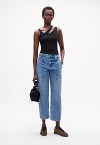 Bodysuit negro de canalé, jeans de mezclilla anchos azules con bolsillos frontales, bolso negro y zapatillas con estampado. Diseño simple y moderno.