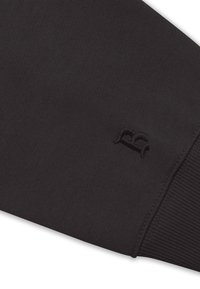 Schwarzes Sweatshirtmaterial mit einer strukturierten Oberfläche. Verfügt über einen gerippten Bund und ein besticktes Logo in passendem dunklem Faden.