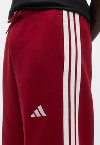 Κόκκινο παντελόνι φόρμας από βαμβάκι, με τρεις λευκές ρίγες στα πλάγια και μικρό λευκό λογότυπο στο μηρό. Περιλαμβάνει ελαστική μέση.