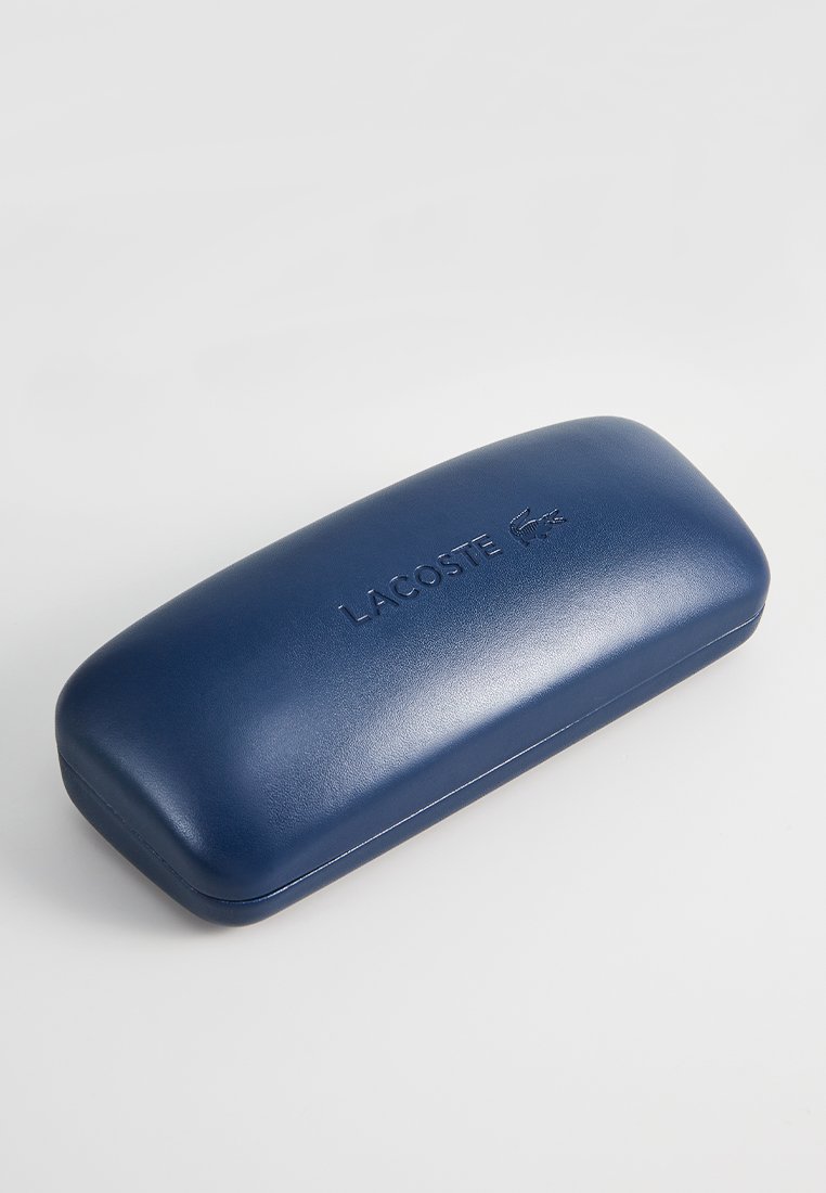 Étui à lunettes rigide bleu marine avec une texture lisse, arborant un logo "LACOSTE" en relief et des bords arrondis pour un aspect élégant.