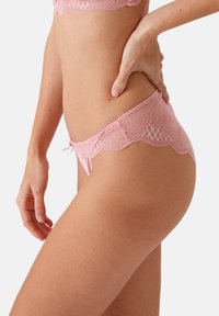 Roze kanten string met golvende randen, voorzien van ingewikkelde bloempatronen en een klein strikje aan de voorkant. Zachte, doorschijnende textuur.