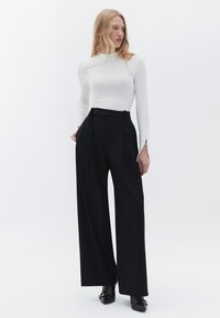 Zwarte wijde broek met een tailored fit, voorzien van een knoopsluiting en een bijpassende riem, gecombineerd met een wit, geribd langslavend shirt.