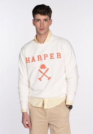 Sudadera blanca con "HARPER" en letras naranjas y gráfico de herramientas cruzadas. Lleva una camisa de cuello amarilla clara debajo. Pantalones beige visibles.