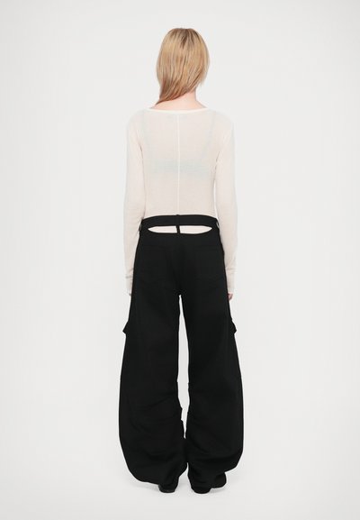 Camisola de mangas longas, de um tom bege claro, com um detalhe de costa aberta, combinada com calças cargo pretas oversized com bolsos laterais e um corte descontraído.