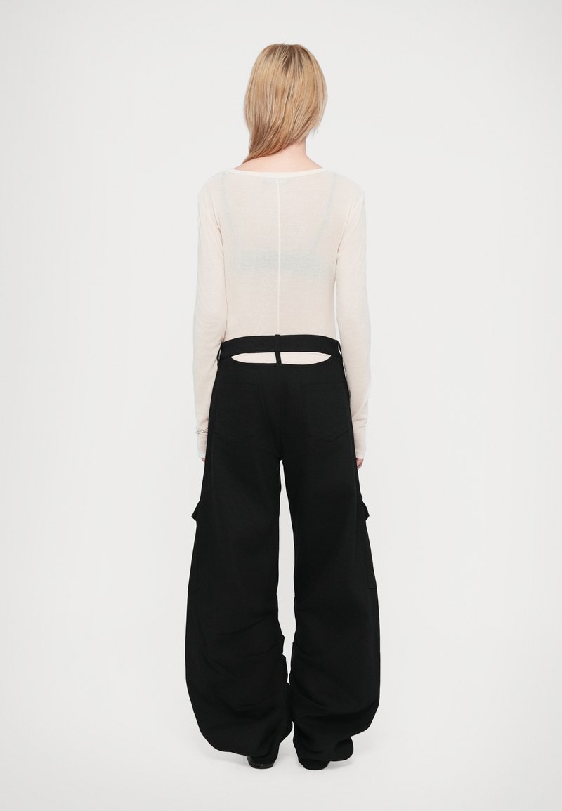 Lange mouwen, licht beige top met een splijt achterkant detail, gecombineerd met oversized zwarte cargobroek met zijzakken en een relaxte pasvorm.