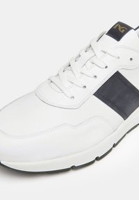 Scarpa da ginnastica bianca con tomaia in pelle liscia, striscia laterale blu navy e lacci tondi. La suola è bianca con un accento nero.