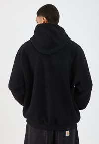 Czarny polarowy bluza z kapturem o teksturowanej powierzchni, w oversize'owym kroju i z regulowanym kapturem. Szczegóły z ribbowanym wykończeniem przy mankietach i dole.