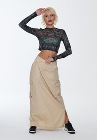 Sort langærmet crop top med multicolorede blomster- og dyremotiver, parret med en beige maxiskirt med cargo-lommer og sideslids.