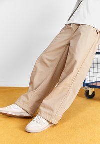 Beiga vida byxor i lätt tyg, med en avslappnad passform och sömnadsdetaljer, som matchas med vita sneakers.