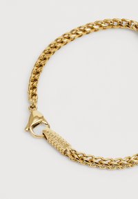 Gullkjedet armbånd med sammenkoblede curb-design, med en lukking i form av krabbe og et merke gravert med "GUESS." Glatt og blank overflate.