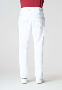 Pantaloni in denim bianco con fit slim. Caratterizzati da cinque tasche, una texture liscia e una leggera elasticità. Indossati con sneakers bianche.