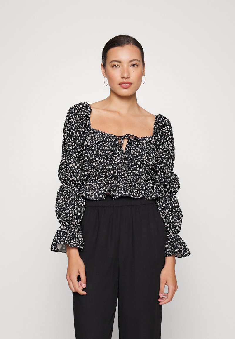 Blusa preta com estampa floral, decote quadrado, mangas bufantes e bainha elástica. Apresenta pequenos padrões florais brancos e rosas. Textura de tecido suave.