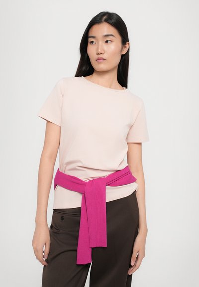 Light pink crew neck t-shirt made of soft cotton, paired with dark brown pants. A bright pink sweater is tied around the waist.