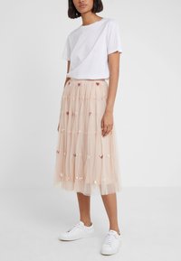 Vrouw in een witte t-shirt gestoken in een beige midi tule rok met sequin hartpatronen, gecombineerd met witte sneakers.