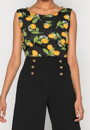 Ærmeløs sort top med gult citron- og grønt bladprint kombineret med sorte bukser med høj talje, der har to lodrette rækker af gyldne knapper.