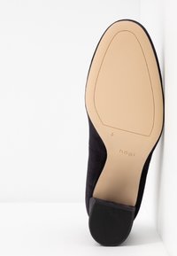 Escarpin en daim noir à bout arrondi, avec une semelle intérieure beige et un talon en caoutchouc texturé. Logo embossé sur la semelle.