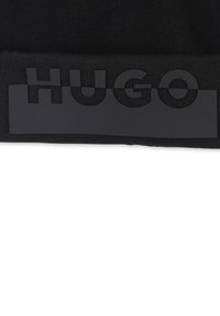Zwarte gebreide beanie met een matte zwarte band waarop het woord "HUGO" staat in vet, moderne typografie. Zachte textuur, goede pasvorm.