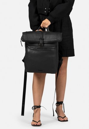 Sac à dos en cuir noir avec un design à rabat, des bretelles ajustables et une texture lisse. Il dispose d'une fermeture par boucle et d'un logo en relief.