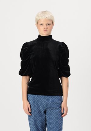 Black velvet top with a high neck and puffed sleeves. Features smooth texture and elegant silhouette, paired with patterned blue pants.