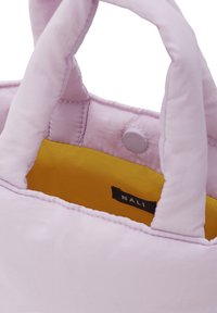 Lys rosa tote bag med polstret tekstur, der har to håndtag, en trykknaplukning og et gult interiør. Etiketten er synlig indeni.
