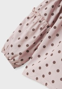 Manica in tessuto rosa con dettaglio arricciato, caratterizzata da pois marroni, texture liscia e cucitura diretta all'orlo.