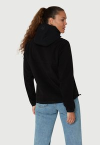 Sort hættejakke med en bl�ød tekstur, der har en indsnævret kant og elastiske manchetter. Ryggen viser et cirkulært logo. Sammen med lyseblå jeans.