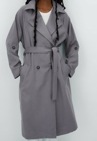 Grau trenchcoat mit tailliertem Gürtel, großen Revers, Seitentaschen und geknöpften Manschetten. Hergestellt aus glattem, leichtem Stoff.