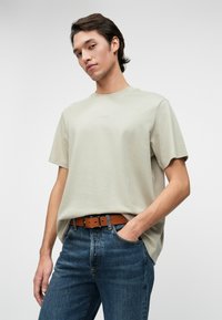 Light gray cotton t-shirt with a round neckline, short sleeves, and subtle branding. Worn with blue denim jeans and a brown belt.