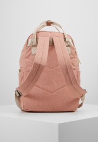 Sac à dos en tissu rose avec un design matelassé, des bretelles beiges réglables, des poches latérales et une poignée supérieure pour le transport.